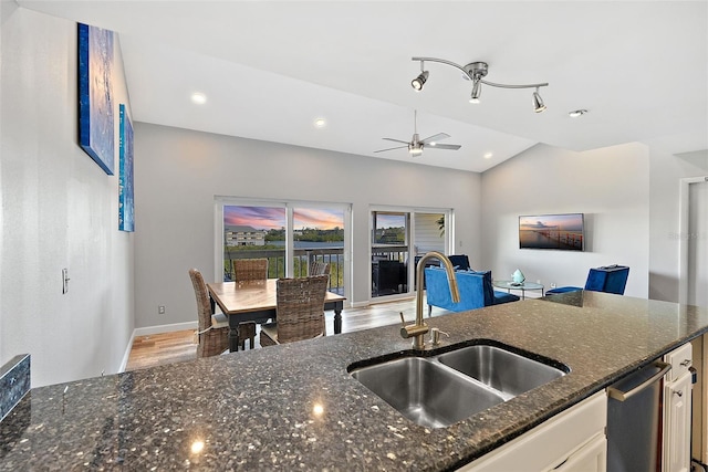 kitchen featuring lofted ceiling, white cabinetry, a sink, wood finished floors, and dark stone counters