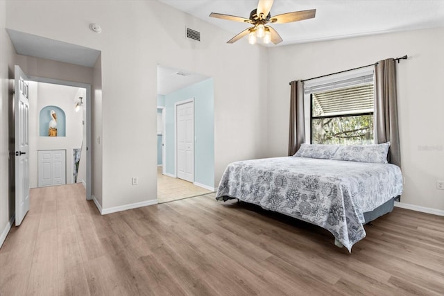 bedroom featuring ceiling fan, visible vents, baseboards, vaulted ceiling, and light wood-style floors