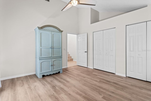 unfurnished bedroom featuring multiple closets, light wood-style floors, baseboards, and ceiling fan