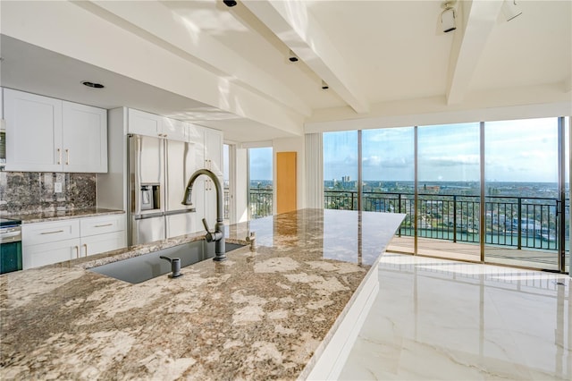 kitchen with decorative backsplash, a sink, light stone countertops, white cabinetry, and beam ceiling