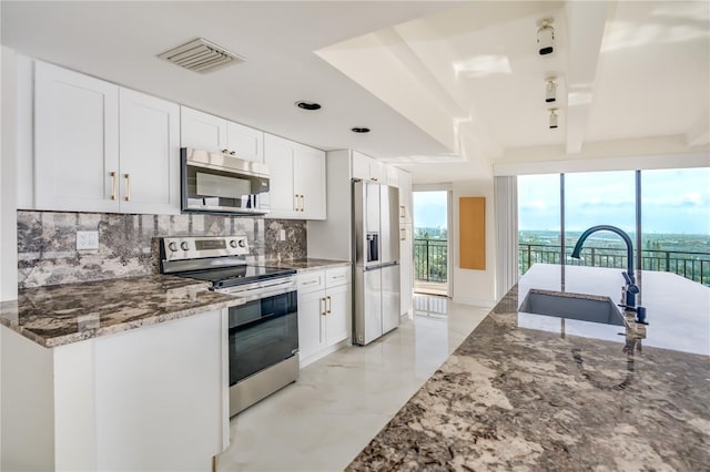 kitchen featuring visible vents, appliances with stainless steel finishes, white cabinetry, a sink, and dark stone countertops