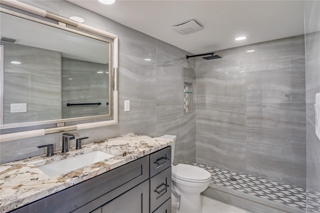 full bathroom with visible vents, toilet, a tile shower, vanity, and tile walls