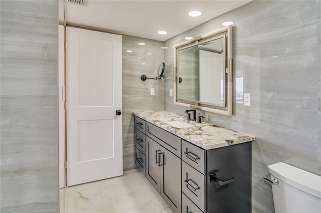 half bathroom featuring toilet, vanity, tile walls, and recessed lighting