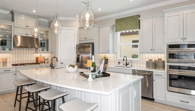 kitchen with appliances with stainless steel finishes, light countertops, a kitchen island with sink, and under cabinet range hood