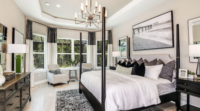 bedroom featuring light wood finished floors, a tray ceiling, a chandelier, and baseboards