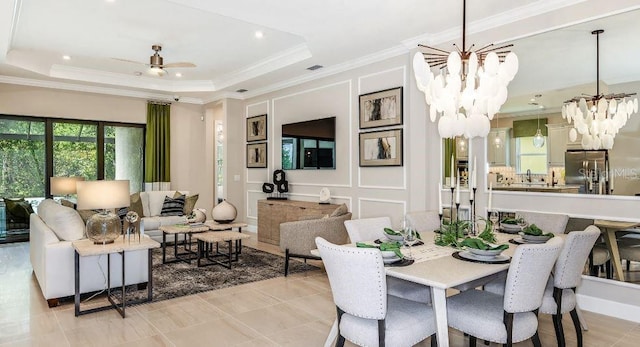 dining area with ceiling fan with notable chandelier, a tray ceiling, a decorative wall, and ornamental molding