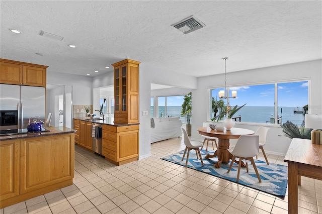 kitchen with decorative light fixtures, stainless steel appliances, a water view, visible vents, and glass insert cabinets