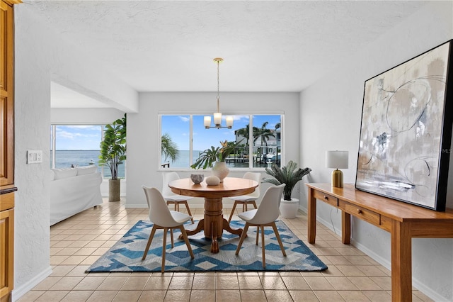 dining space with baseboards, a water view, a textured ceiling, a notable chandelier, and light tile patterned flooring