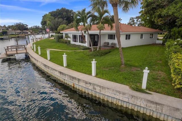 back of property with a water view, a lawn, a tiled roof, and stucco siding