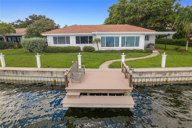 back of property with a water view, stucco siding, a tiled roof, and a yard