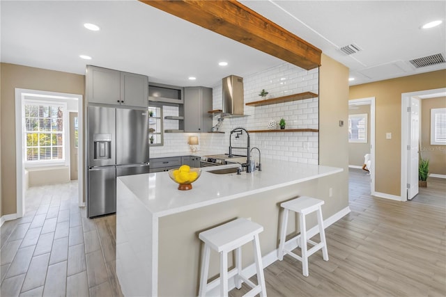 kitchen featuring tasteful backsplash, wall chimney exhaust hood, visible vents, stainless steel refrigerator with ice dispenser, and gray cabinetry