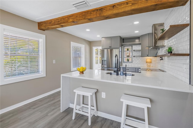 kitchen featuring open shelves, stainless steel fridge, a sink, gray cabinetry, and wall chimney exhaust hood