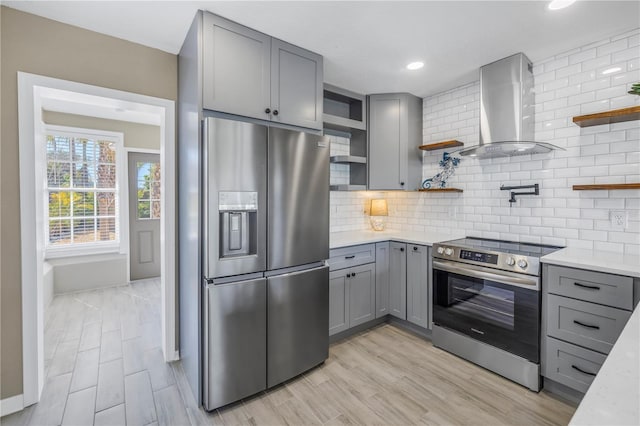 kitchen with appliances with stainless steel finishes, gray cabinetry, open shelves, and wall chimney range hood