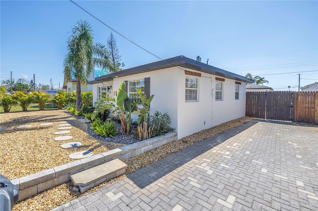 view of side of home with stucco siding, fence, and a patio
