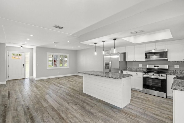 kitchen with appliances with stainless steel finishes, open floor plan, white cabinetry, a kitchen island, and dark stone countertops