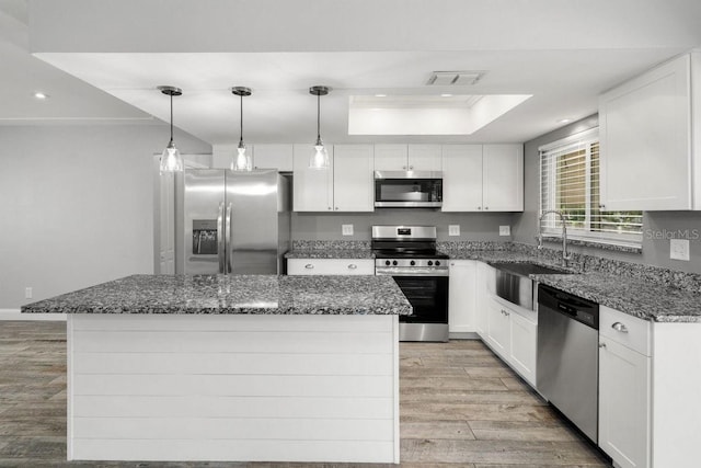 kitchen featuring stainless steel appliances, white cabinetry, a kitchen island, and a sink