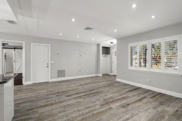 unfurnished living room with a barn door, wood finished floors, visible vents, and recessed lighting