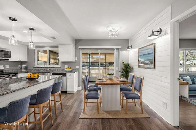 dining space featuring a raised ceiling, visible vents, dark wood finished floors, and wooden walls