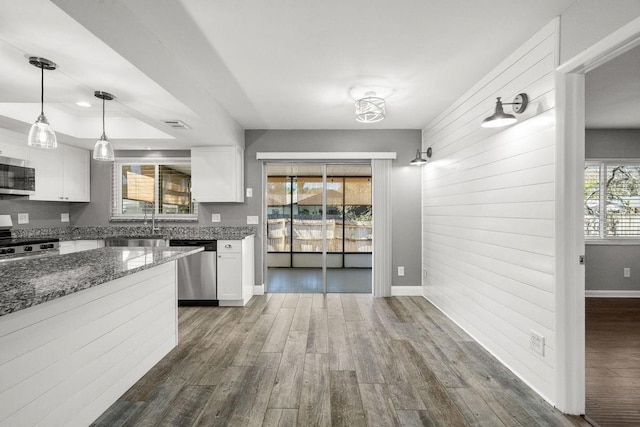 kitchen with dark wood-style flooring, stainless steel appliances, a raised ceiling, white cabinets, and dark stone countertops