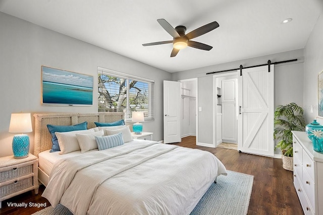 bedroom featuring a barn door, baseboards, ceiling fan, dark wood-type flooring, and a spacious closet