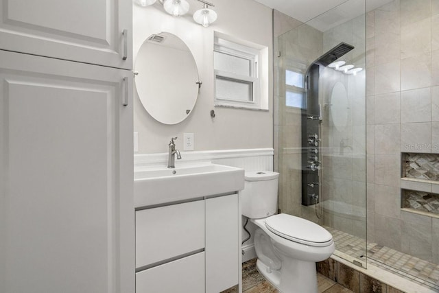 full bathroom with a shower stall, a wainscoted wall, vanity, and toilet