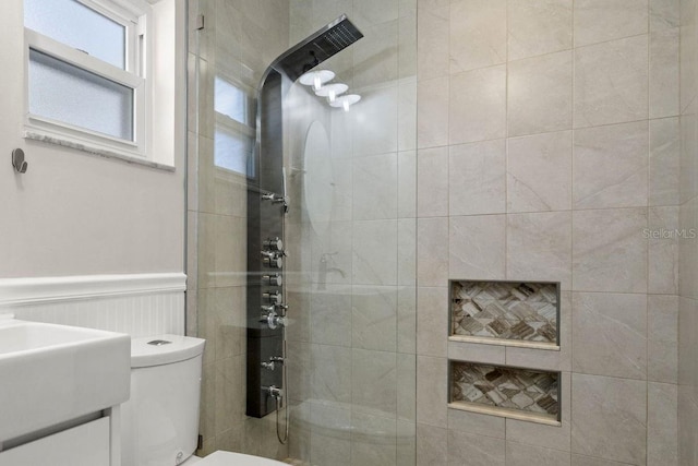 bathroom featuring a wainscoted wall, vanity, a walk in shower, and toilet