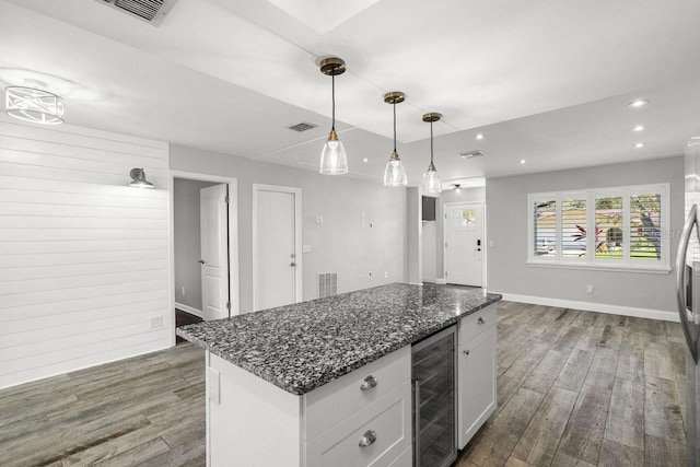 kitchen with beverage cooler, dark stone countertops, decorative light fixtures, a center island, and white cabinetry