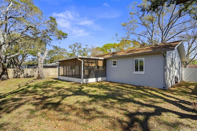 back of house featuring a sunroom, a fenced backyard, a lawn, and stucco siding