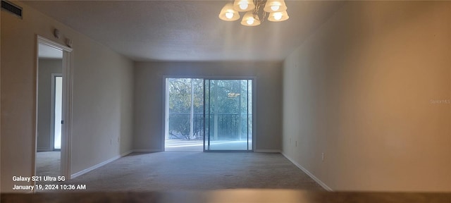 unfurnished room with visible vents, an inviting chandelier, light carpet, a textured ceiling, and baseboards