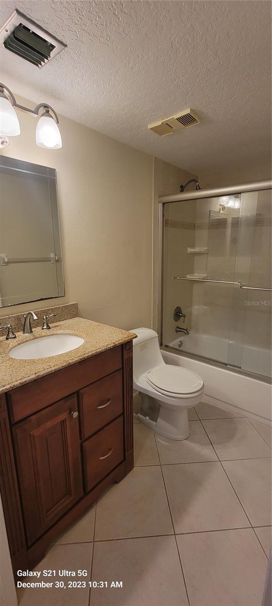 full bathroom featuring visible vents, toilet, combined bath / shower with glass door, and tile patterned floors