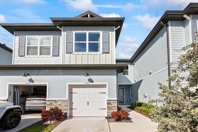 townhome / multi-family property with a garage, stone siding, board and batten siding, and driveway