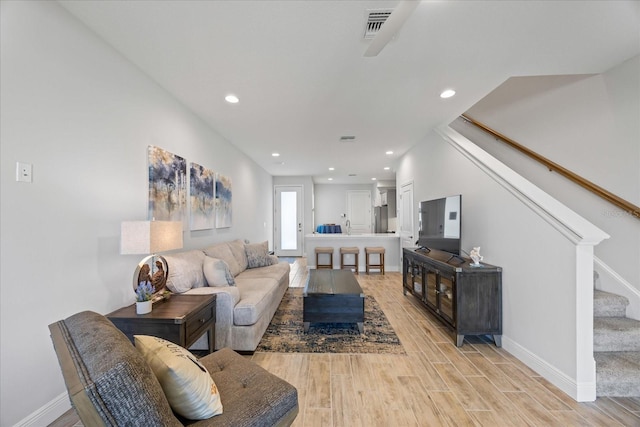 living area with recessed lighting, visible vents, light wood-style flooring, stairway, and baseboards