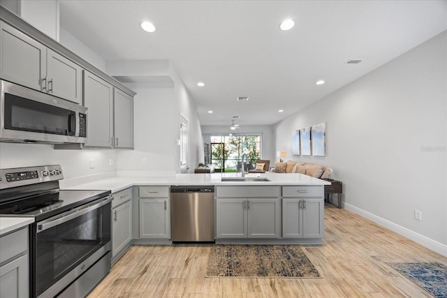 kitchen with appliances with stainless steel finishes, open floor plan, a peninsula, light countertops, and a sink