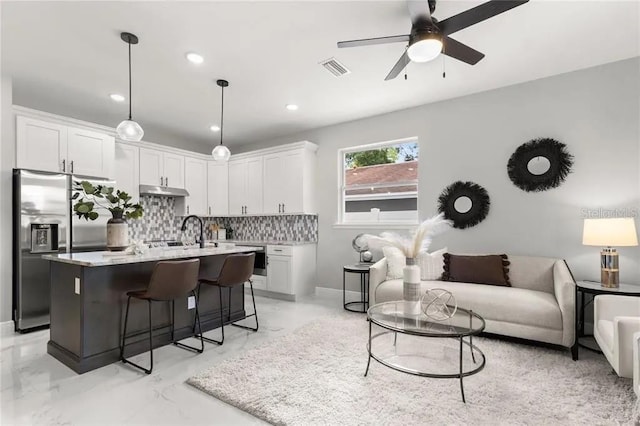 kitchen with a breakfast bar area, open floor plan, marble finish floor, stainless steel refrigerator with ice dispenser, and tasteful backsplash