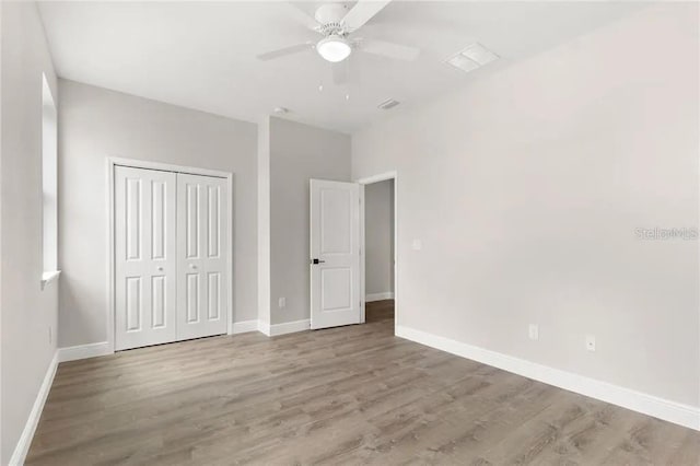 unfurnished bedroom featuring ceiling fan, wood finished floors, visible vents, baseboards, and a closet