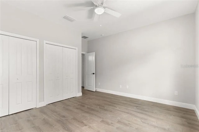 unfurnished bedroom with multiple closets, visible vents, baseboards, and wood finished floors