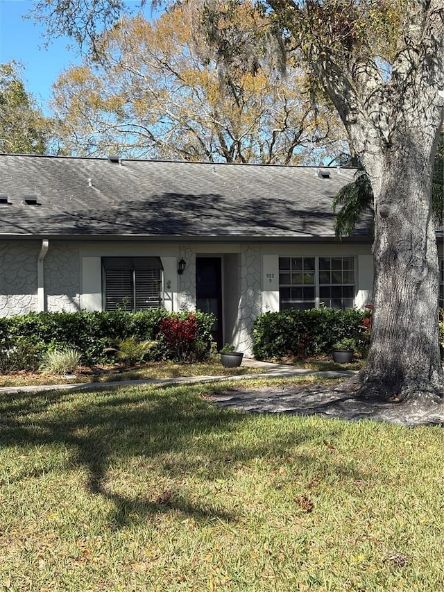 view of front facade featuring stucco siding, a shingled roof, and a front yard