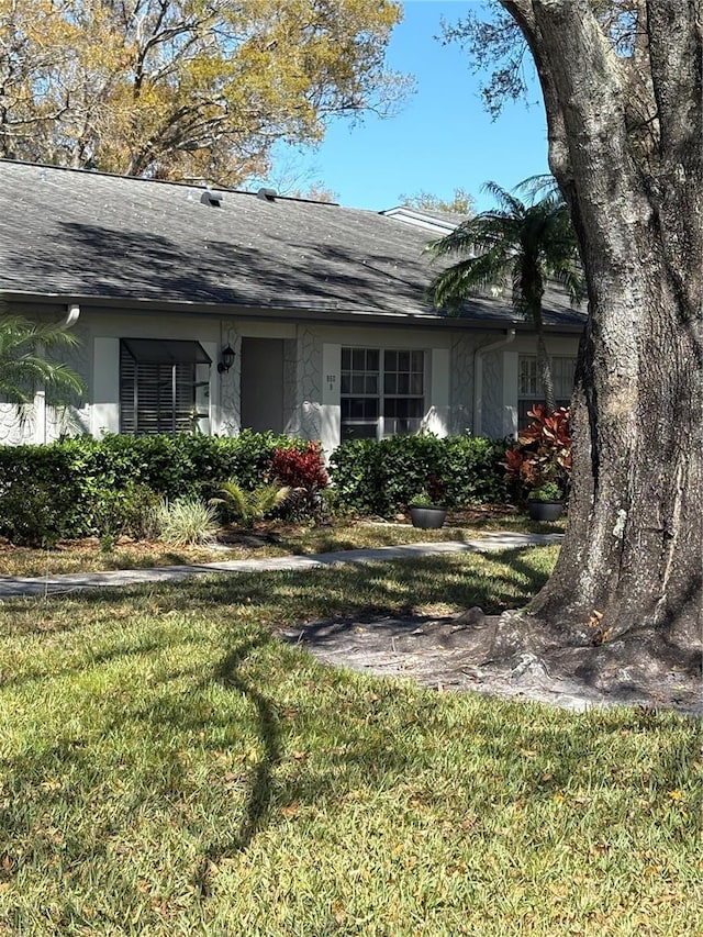 single story home featuring a shingled roof, a front lawn, and stucco siding