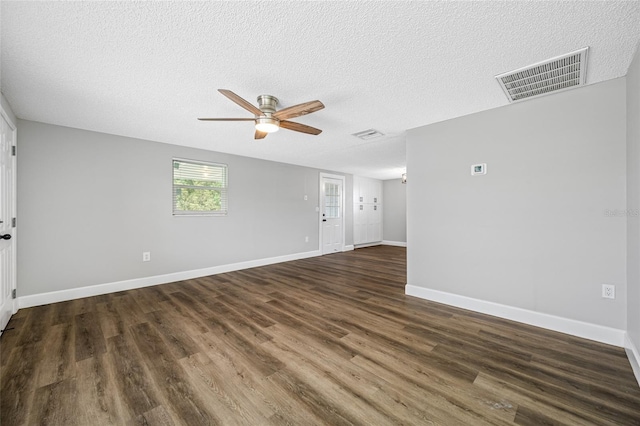 empty room with dark wood-style floors, a textured ceiling, visible vents, and baseboards