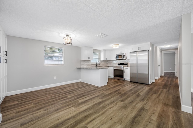 kitchen with a peninsula, appliances with stainless steel finishes, white cabinetry, and decorative backsplash