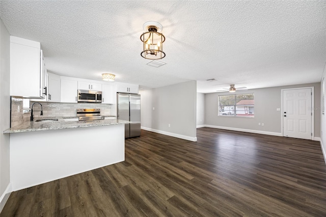 kitchen with a peninsula, a sink, white cabinets, open floor plan, and appliances with stainless steel finishes