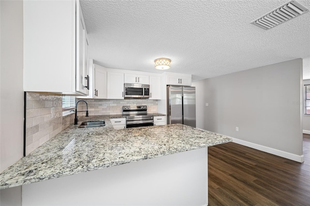 kitchen with appliances with stainless steel finishes, white cabinets, a sink, and a peninsula