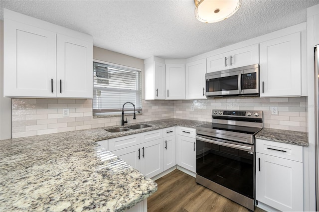 kitchen with appliances with stainless steel finishes, white cabinetry, a sink, and light stone countertops