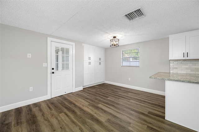 unfurnished dining area featuring dark wood-type flooring, visible vents, and baseboards