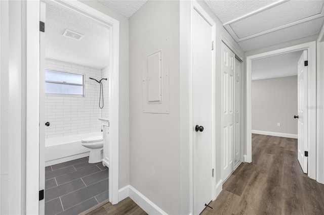 hallway featuring dark wood-style flooring, visible vents, a textured ceiling, and baseboards