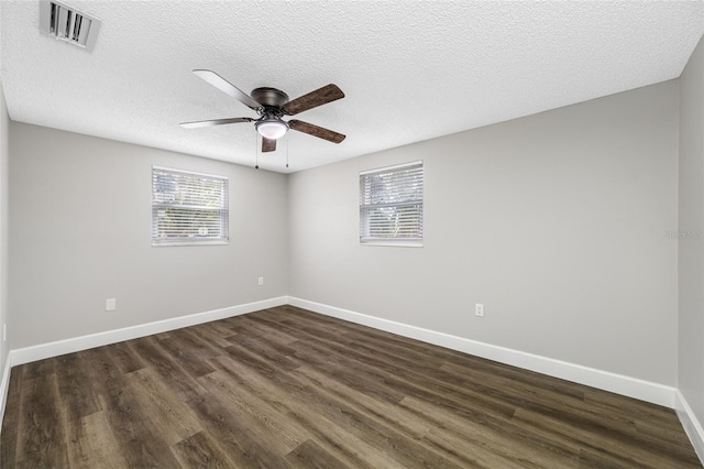 empty room with visible vents, dark wood finished floors, a textured ceiling, and baseboards