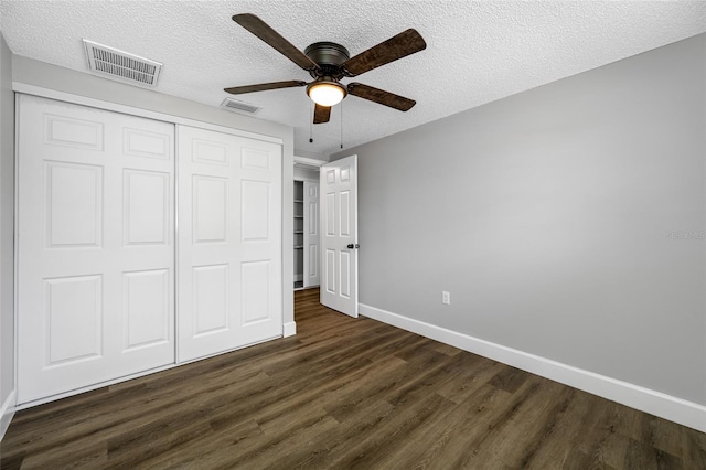 unfurnished bedroom with dark wood-style flooring, a closet, visible vents, a textured ceiling, and baseboards