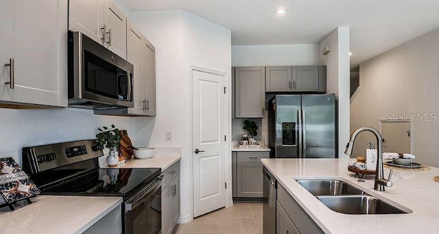 kitchen with appliances with stainless steel finishes, light countertops, a sink, and gray cabinetry