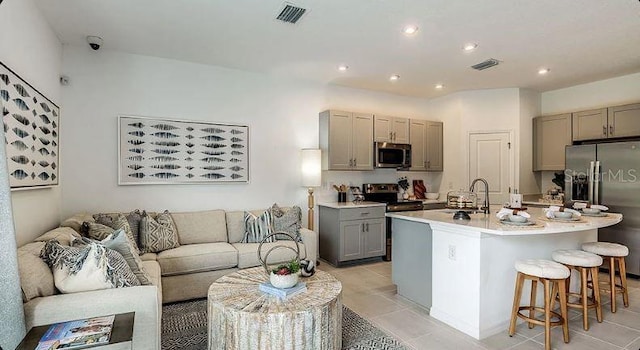 kitchen featuring a center island with sink, gray cabinets, stainless steel appliances, light countertops, and a sink