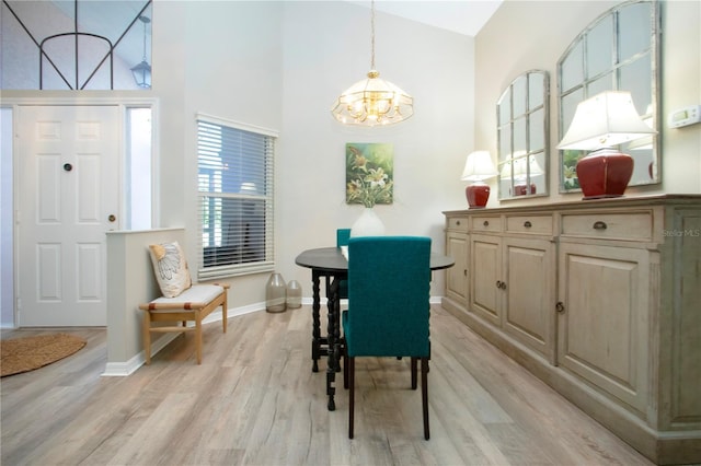 dining area with light wood-type flooring, baseboards, a high ceiling, and a chandelier